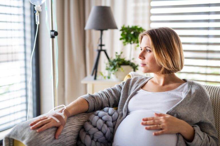 Pregnant woman receiving IV therapy while sitting on a couch.