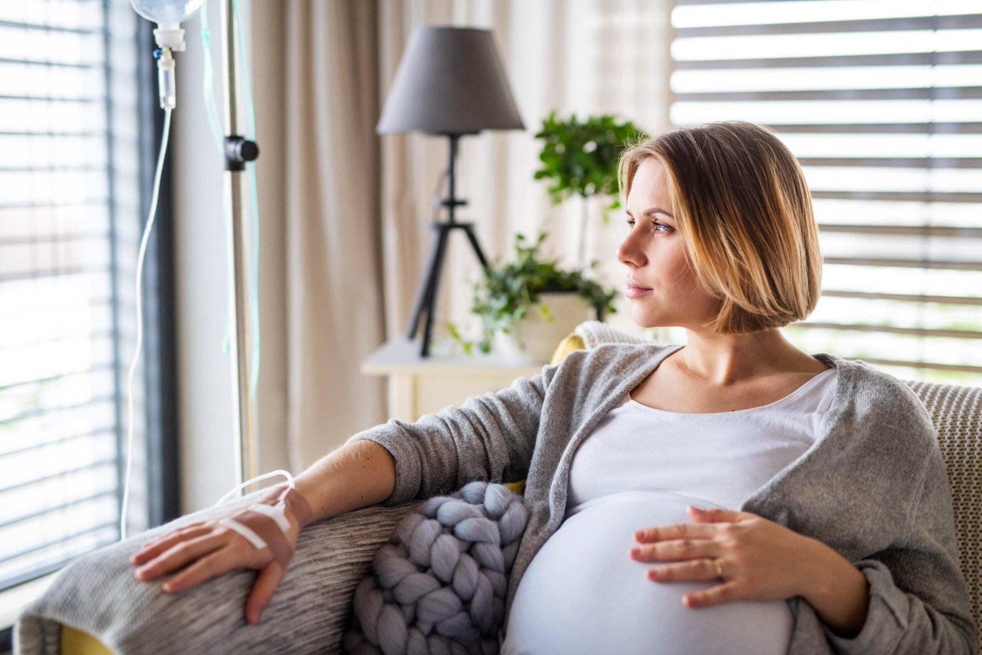 Pregnant woman receiving IV therapy while sitting on a couch.