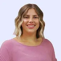 Smiling woman with wavy blonde hair in a pink shirt against a light background.