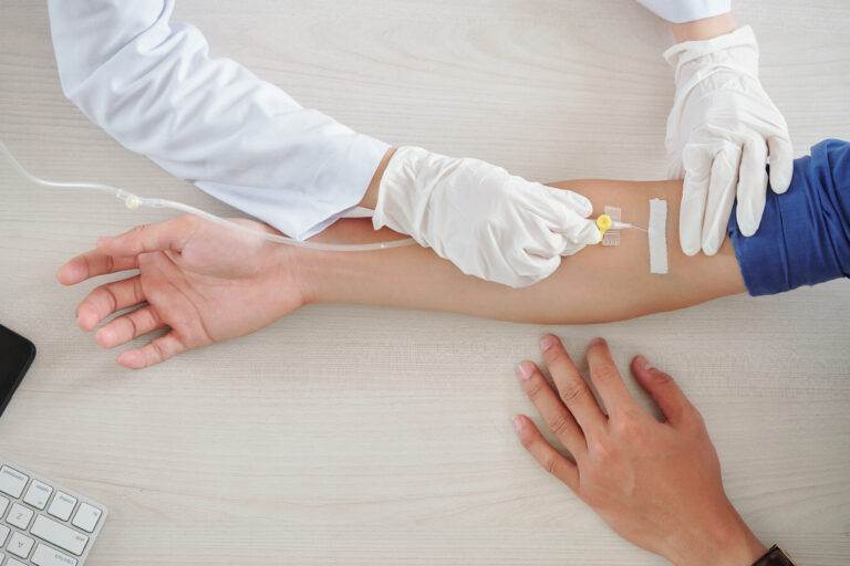 Close-up view of a healthcare professional administering an IV infusion to a patient's arm.