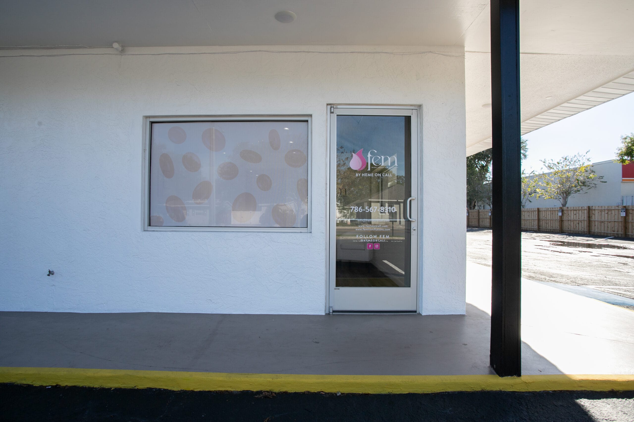 Exterior view of the Infusion Center in Saint Petersburg, Florida, with a white facade and glass door displaying the logo "fem by Heme On Call.