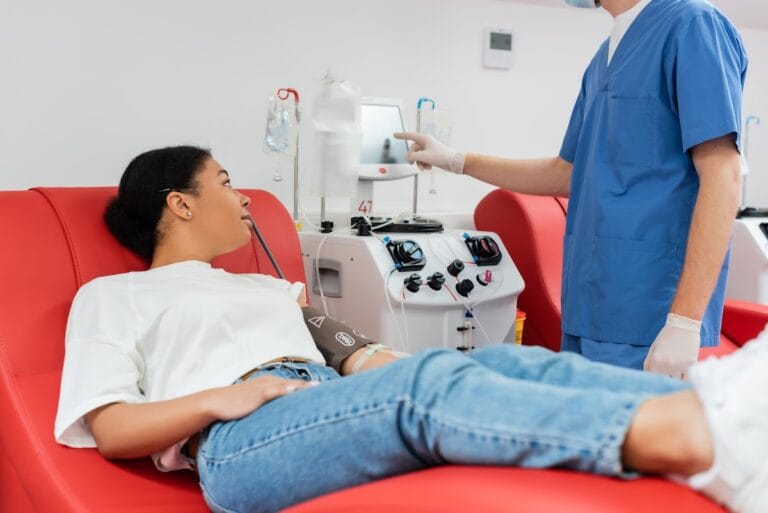 Patient receiving a blood transfusion while reclining in a chair, supervised by a healthcare professional, showcasing modern medical care.