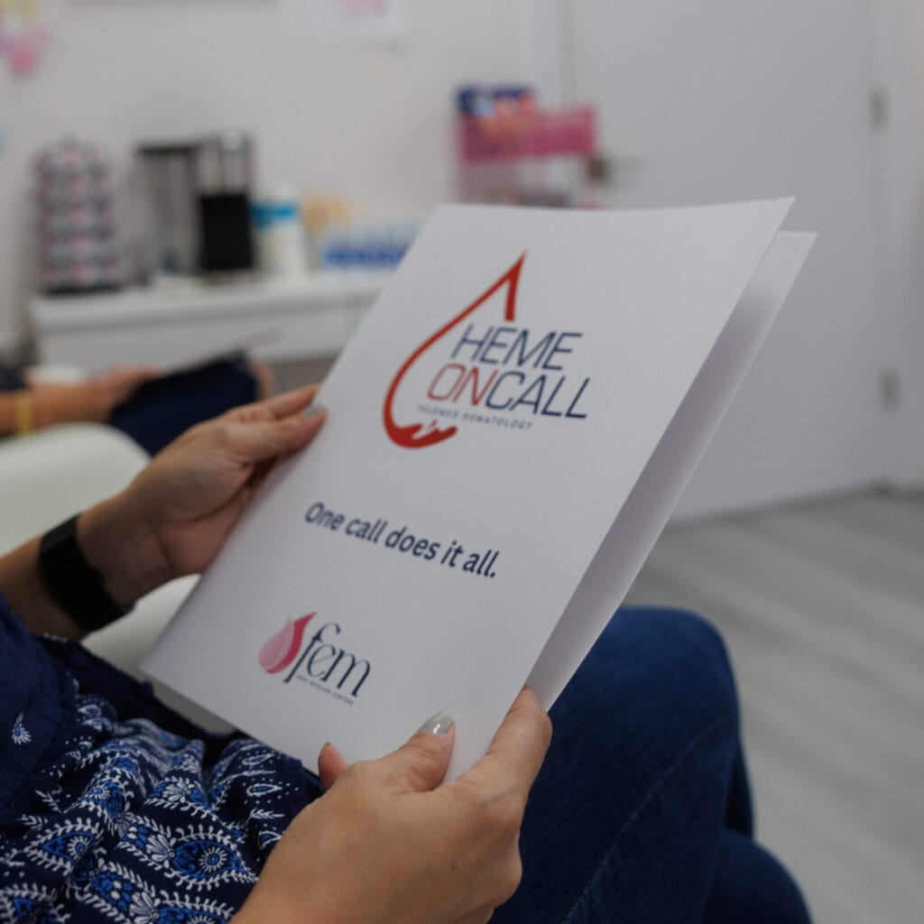Person reading a brochure featuring the Heme On Call logo in a modern office setting.