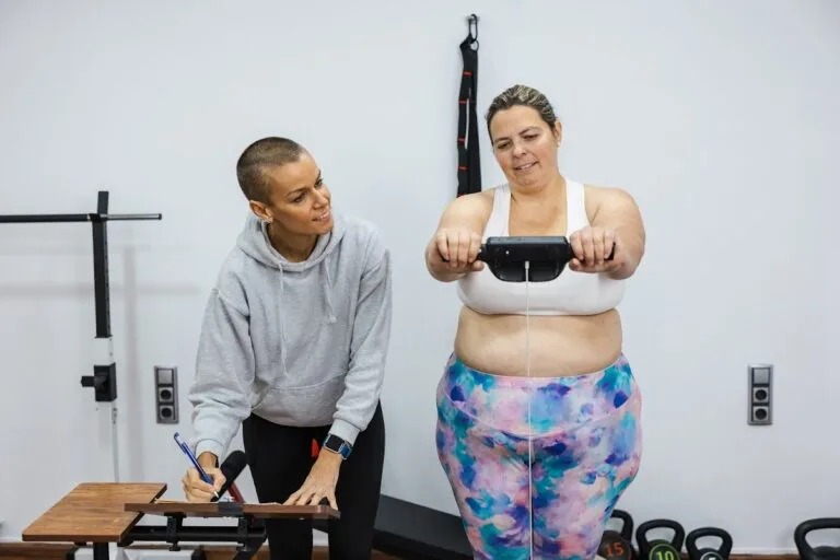Woman using a body composition analyzer while a nutritionist records the results.