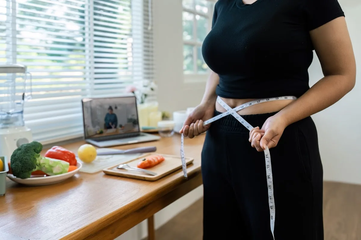 Overweight woman measuring her hips with a tape measure to track weight loss progress.
