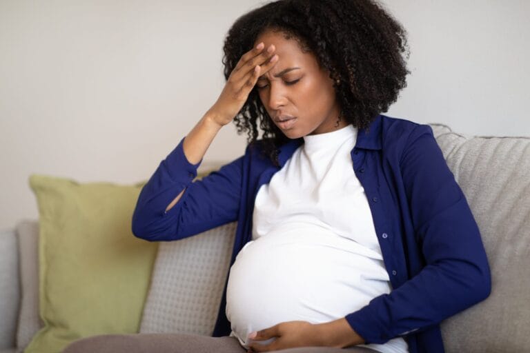 Pregnant woman sitting on couch with headache