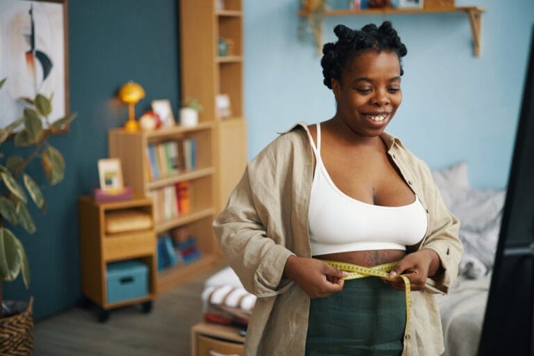 Woman measuring waist with tape at home