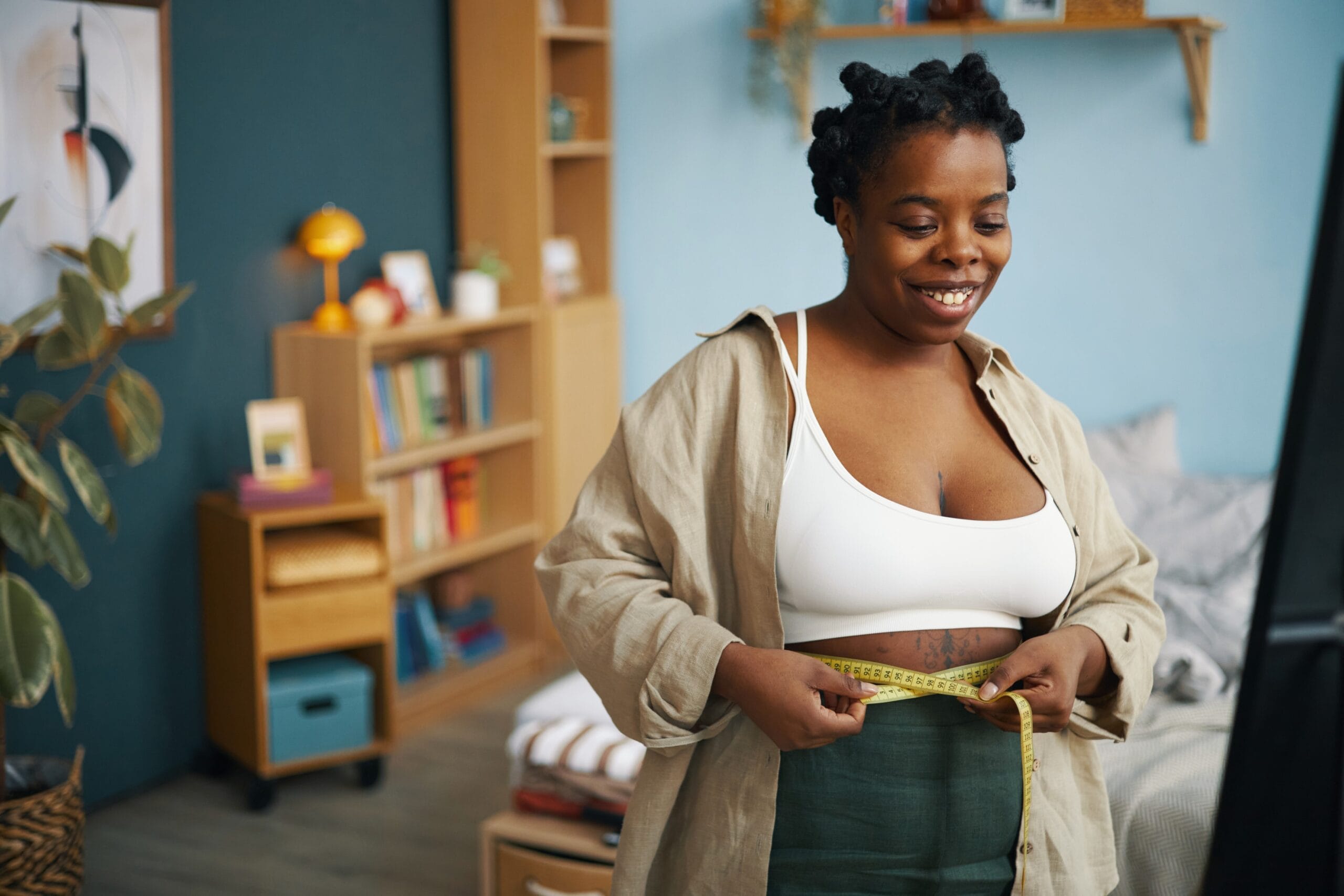 Woman measuring waist with tape at home