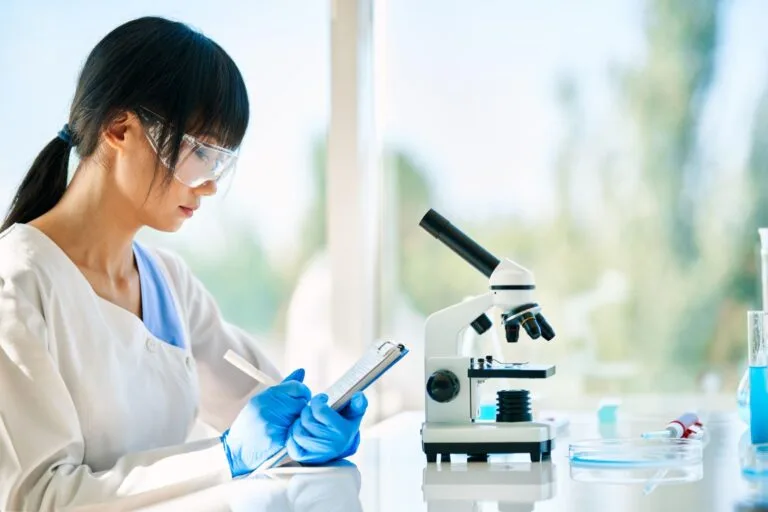 Scientist writing notes near microscope